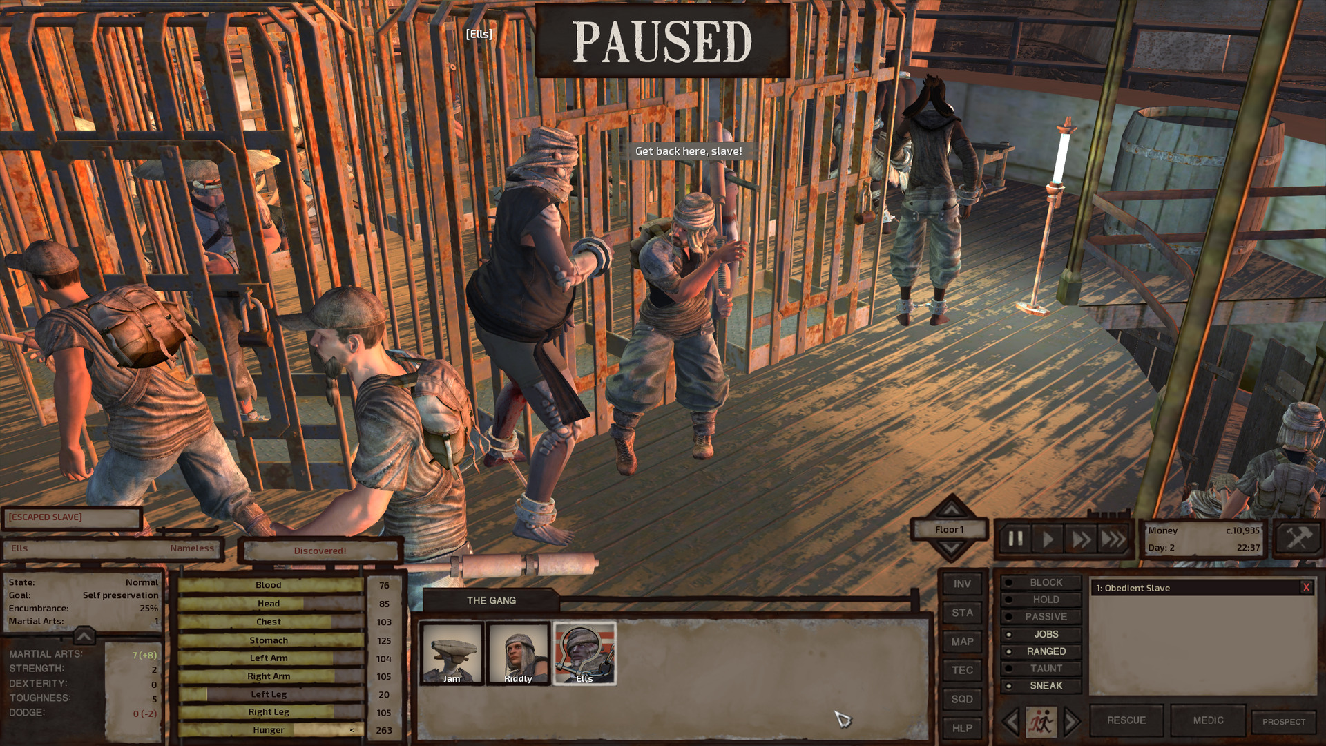Ells, now outside his prison cage but with shackles around his wrists and ankles, flinches as a man attacks him with a club. The man, a member of the Slave Traders faction, yells at him as he does so. Other Slave Traders mill about the room, as does another prisoner who has also now been clapped in irons.